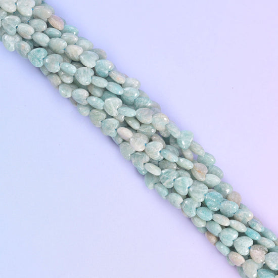 Diagonal run of pale blue Amazonite heart beads across a pastel backdrop