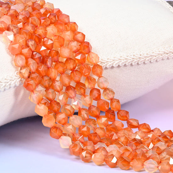 Orange Agate diamond star cut beads, strands laid over white fabric, warm orange banded with translucent cream