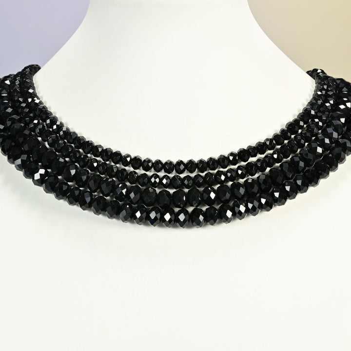 Black onyx beads shown on a white neck display, four faceted rondelle strands layered close to the neckline