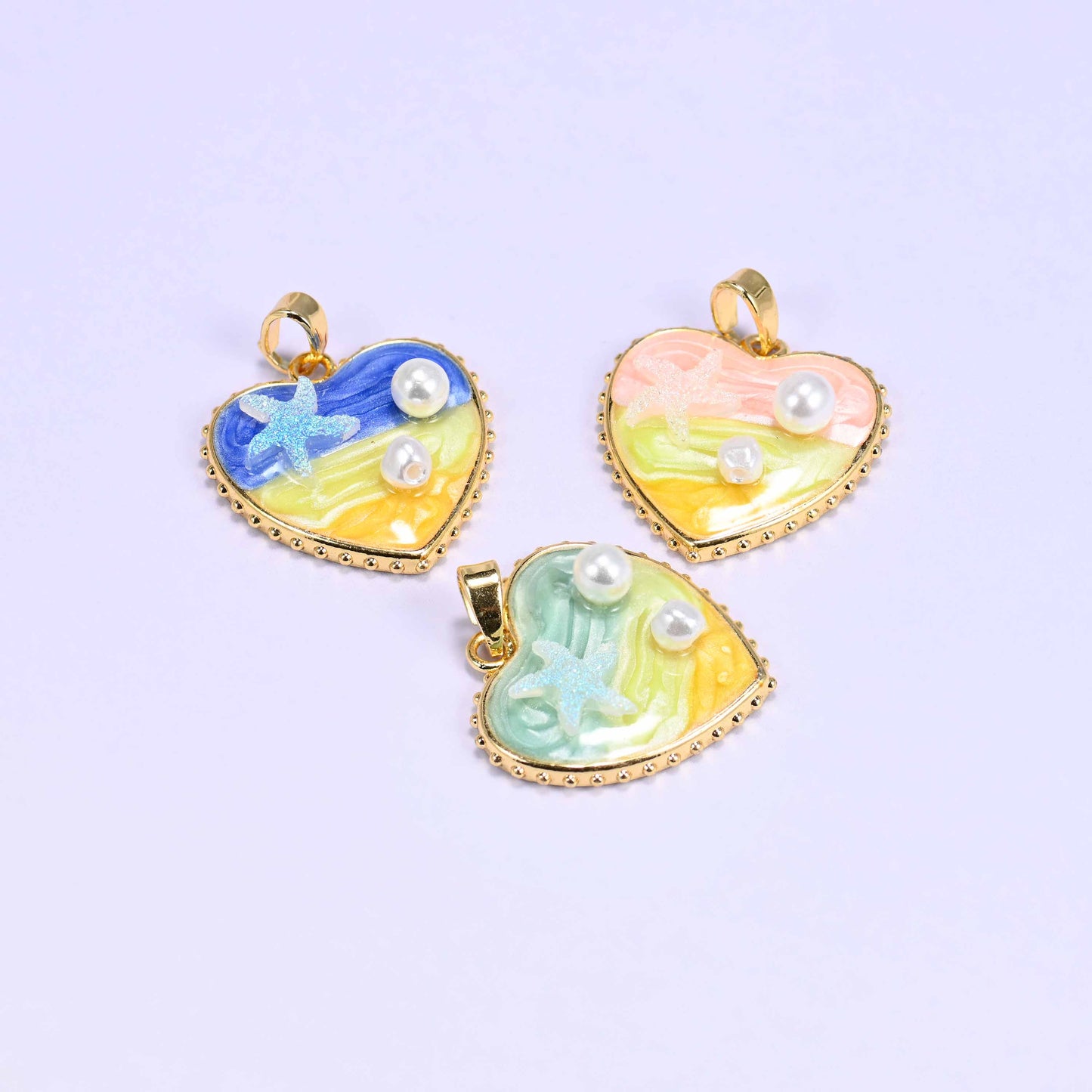 Enamel Heart Pendants shown tilted on their sides, blue and pink above and green below, so the gold plated bail and the depth of the enamel are visible.