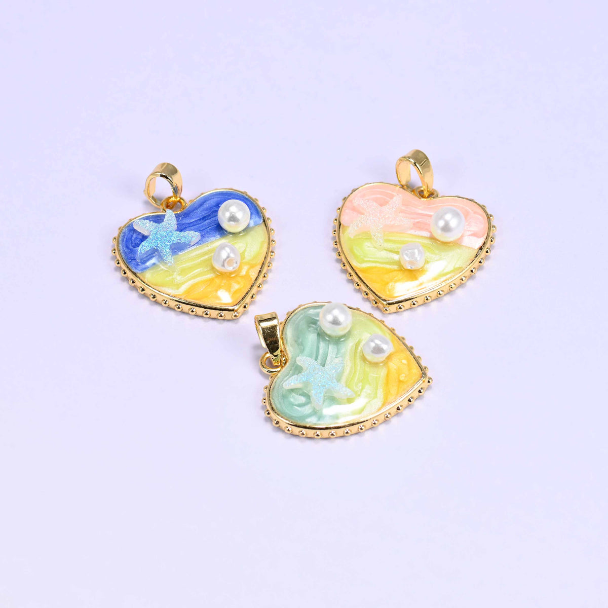 Enamel Heart Pendants shown tilted on their sides, blue and pink above and green below, so the gold plated bail and the depth of the enamel are visible.