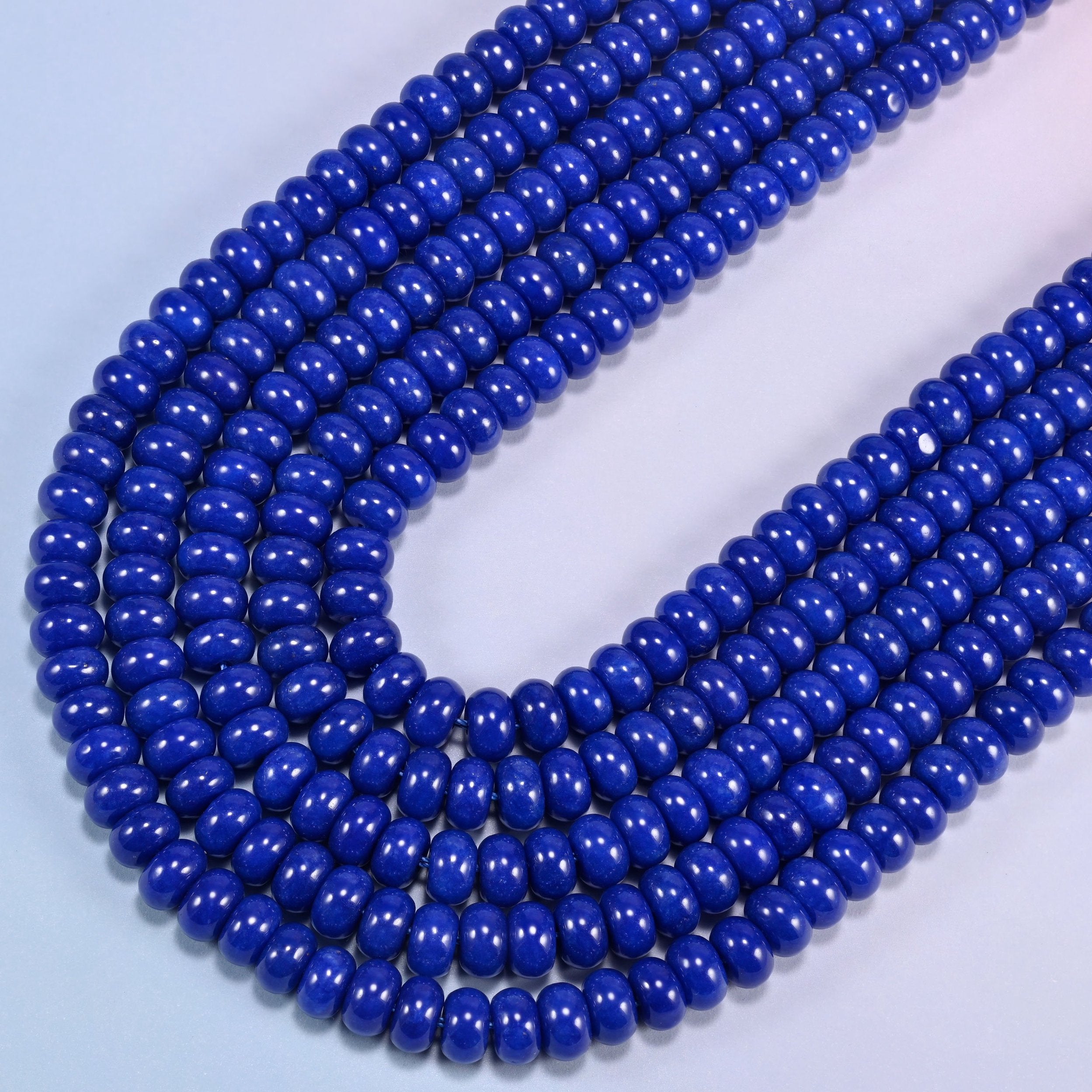 Dark Blue dyed jade gemstone rondelle beads curving in a wide U across the frame, colour even from bead to bead
