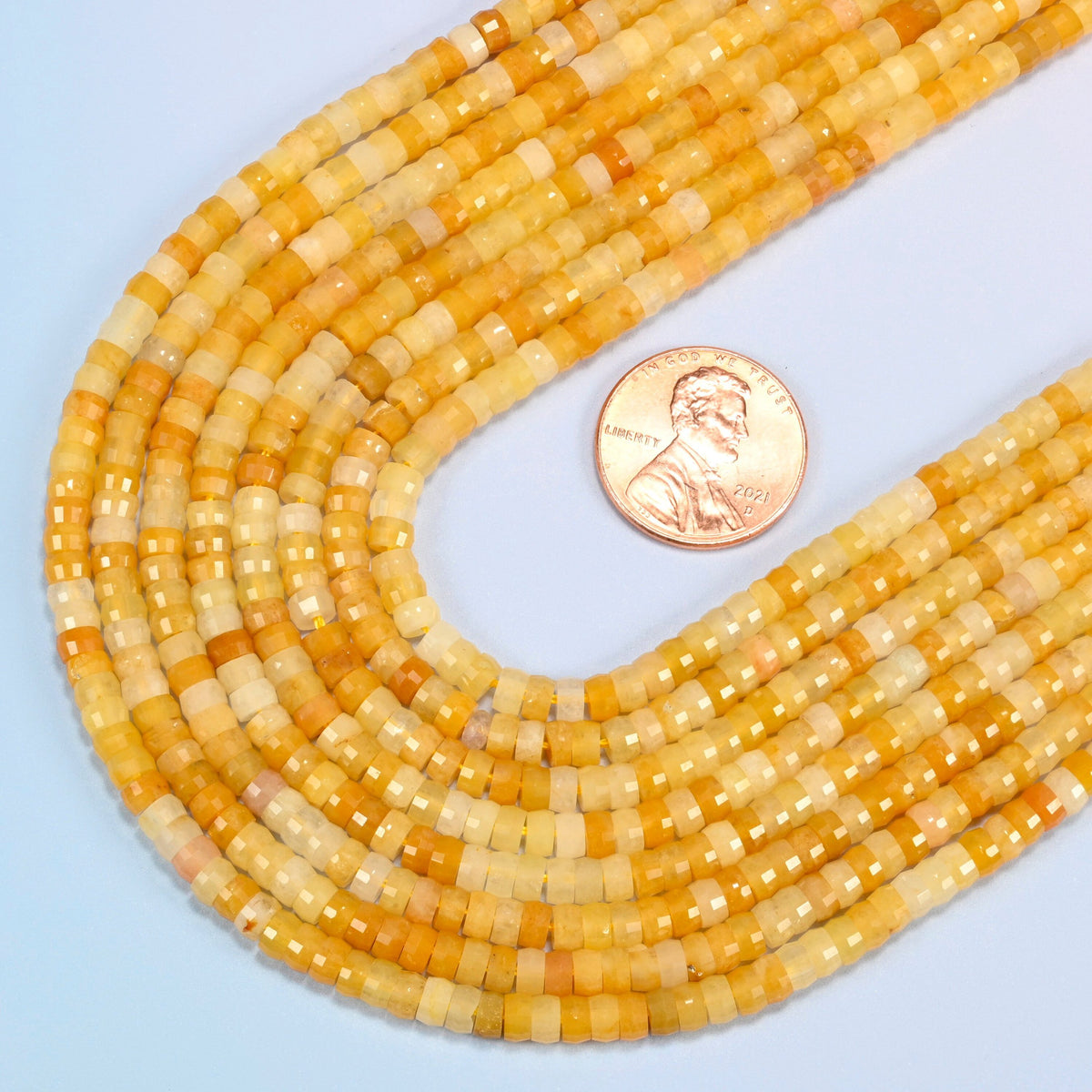 Close view of Gold Silk Jade faceted heishi disc strands curving beside a US penny for scale