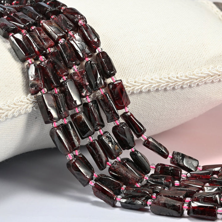 Red garnet tube beads 7x10-7x14mm with small pink seed bead spacers, several strands draped over a white cushion