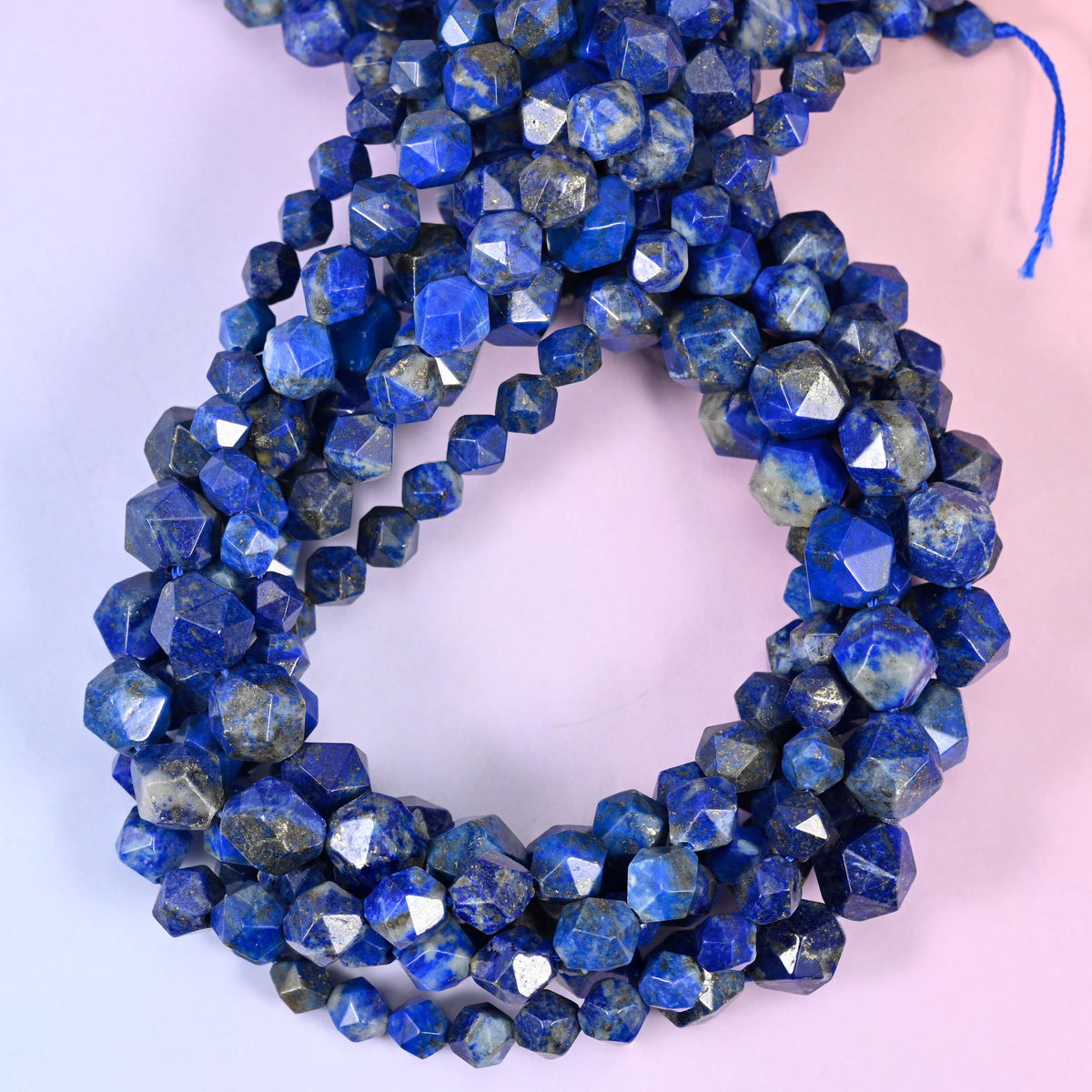 Blue Lapis Lazuli star cut beads coiled in a loop with the blue stringing cord showing, approximately 38 beads per 10mm strand