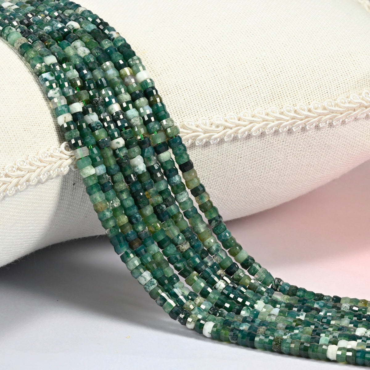 Moss agate faceted heishi disc beads 2x4mm, several strands draped over a white cushion