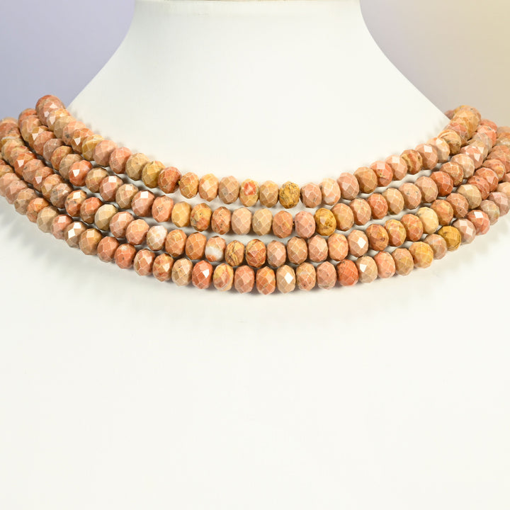 Orange stone faceted rondelle strands arranged as a layered collar on a white display bust, peach orange beads across the neck