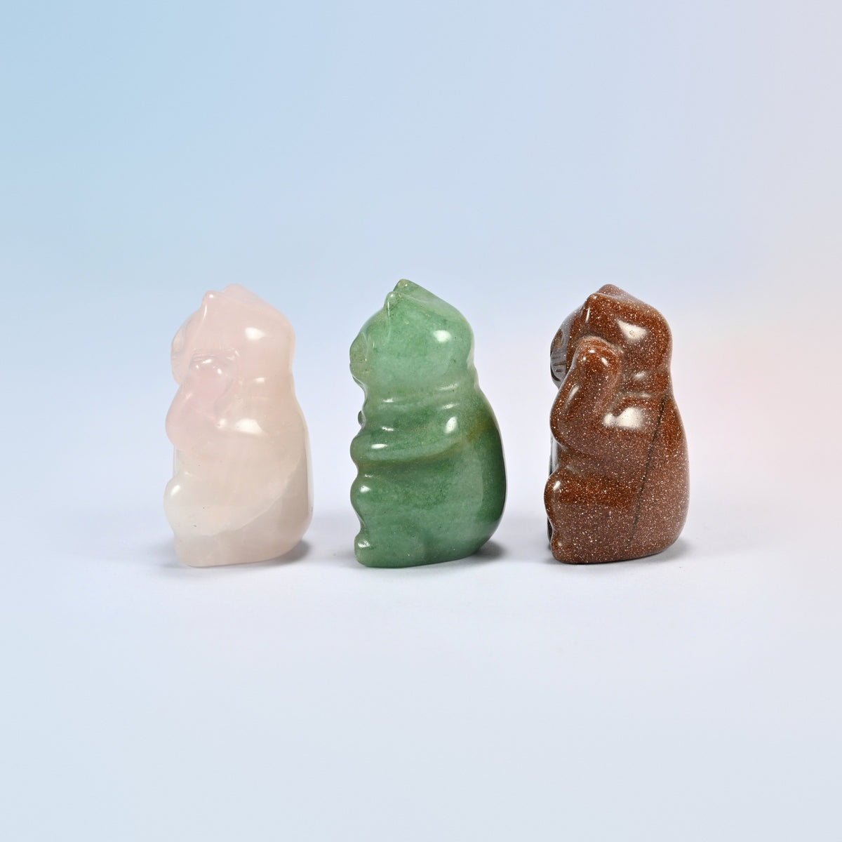 Three small lucky cat carvings in pink, green and sparkly brown stone turned to the side