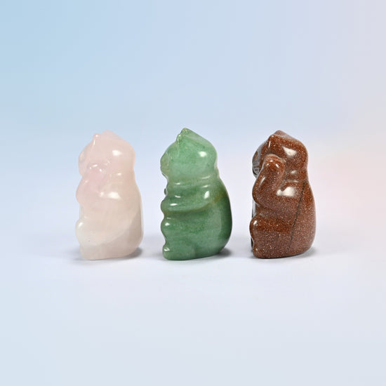 Three small lucky cat carvings in pink, green and sparkly brown stone turned to the side