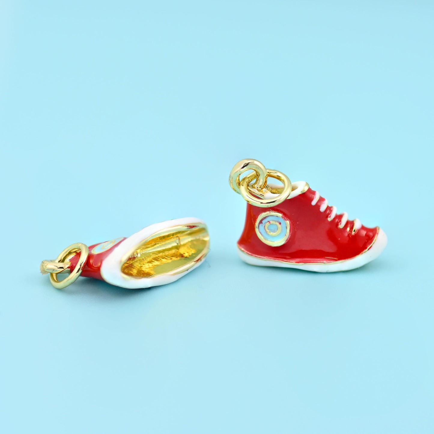 Sneaker pendant in red shown two ways, one upright and one tipped onto its side to reveal the plain gold sole.