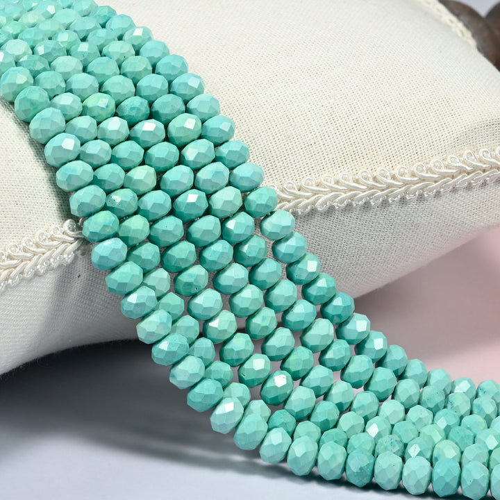 Dyed blue green howlite faceted rondelle beads 5x8mm in soft mint turquoise, several strands draped over a white cushion