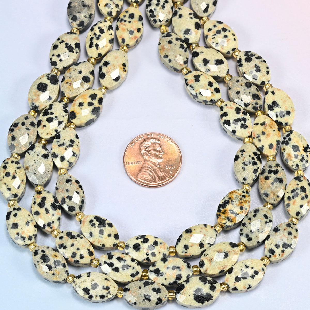 Dalmatian jasper faceted flat oval strands formed into a teardrop loop around a US penny for scale