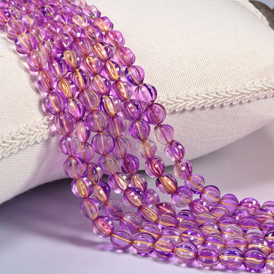 Purple gold pumpkin glass beads, 8mm fluted melon rounds, several strands draped over a white cushion.
