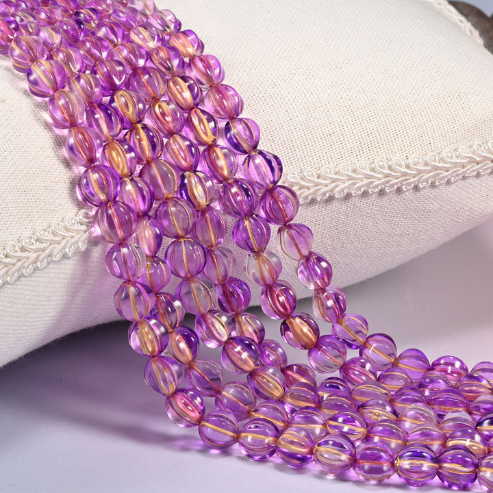 Purple gold pumpkin glass beads, 8mm fluted melon rounds, several strands draped over a white cushion.