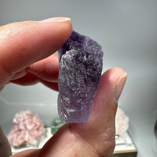 The 0.95 oz fluorite piece pinched between finger and thumb, giving a clear sense of its small size
