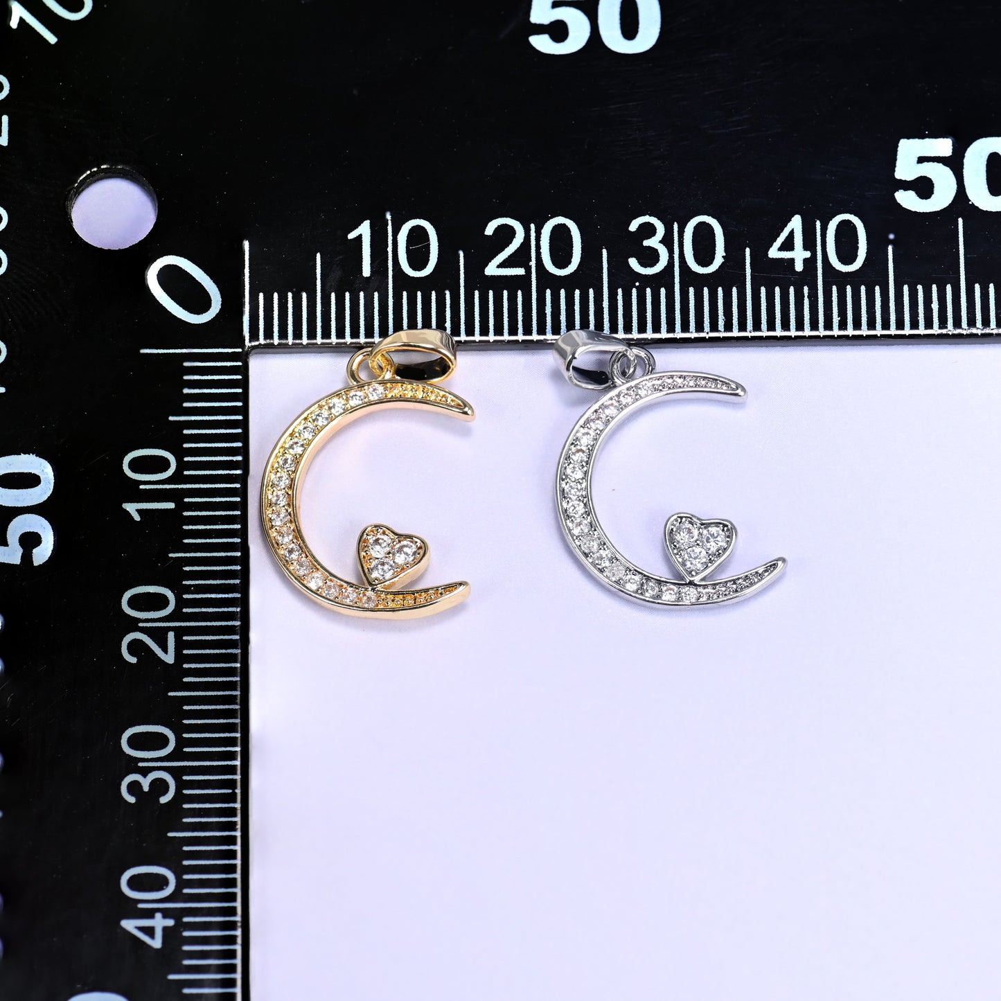 Gold and silver moon heart zirconia charms together on a black millimetre ruler for size reference.
