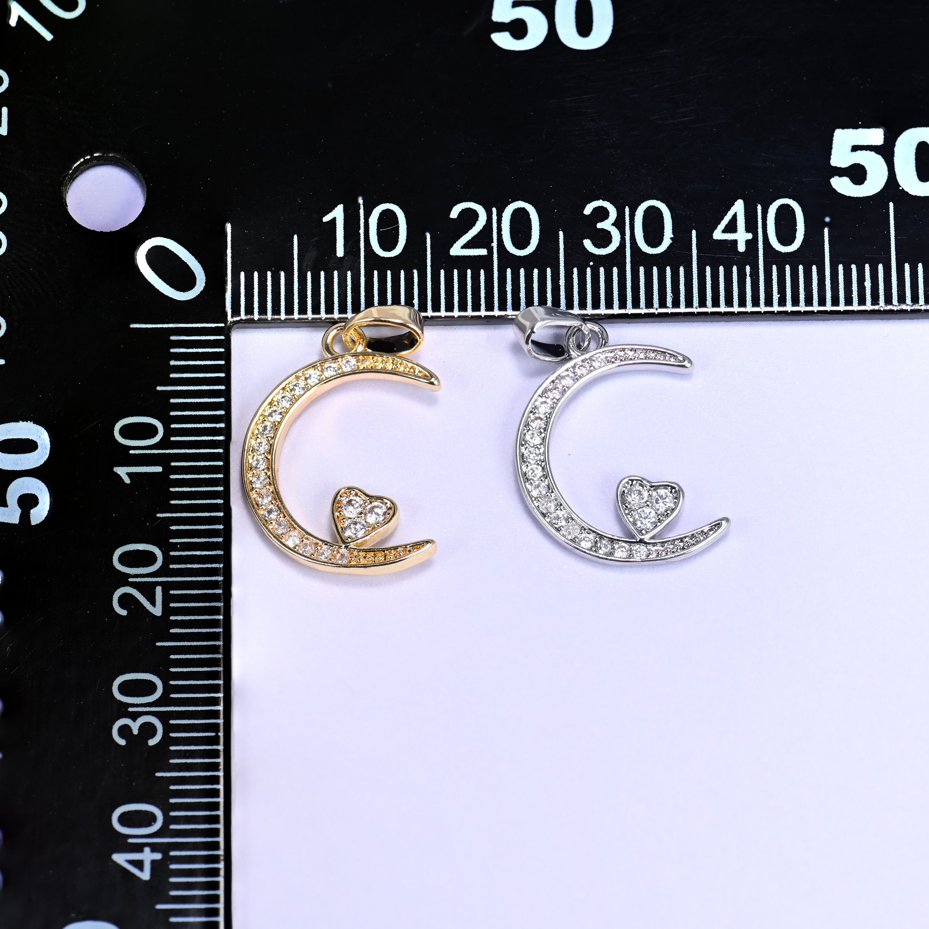 Gold and silver moon heart zirconia charms together on a black millimetre ruler for size reference.