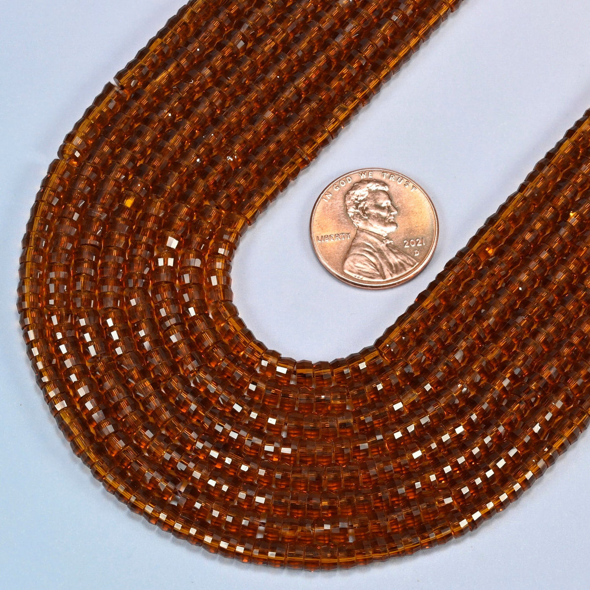 Close view of brown glass faceted heishi disc strands curving beside a US penny for scale