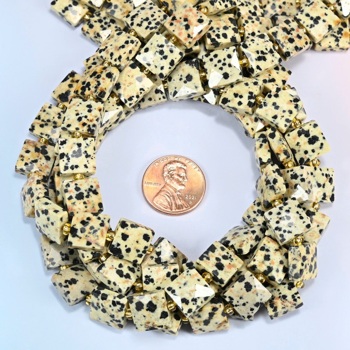 Dalmatian jasper faceted flat square beads 10x10mm coiled in a loop around a US penny for scale, close-up of the faceted flat square shape
