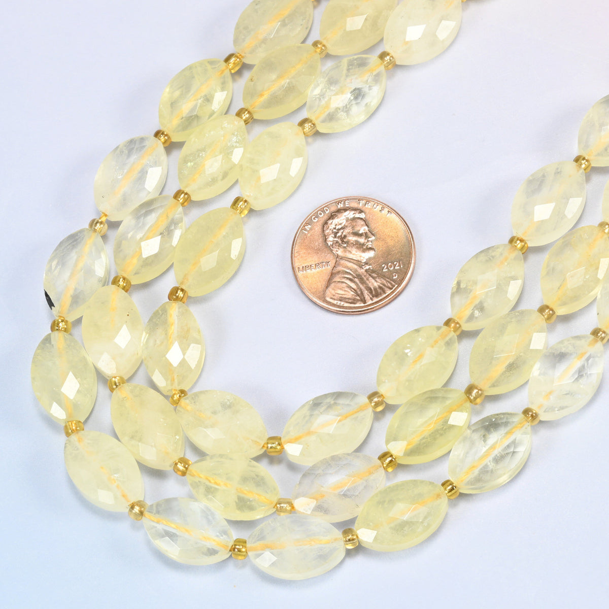 Close view of citrine faceted flat oval strands curving beside a US penny for scale