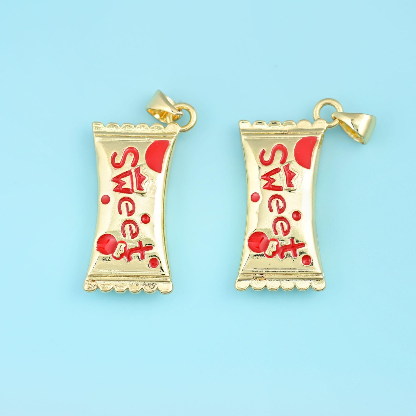 A wrapped sweet with pinched twisted ends, cast in gold filled brass and painted with the word Sweet in glossy enamel — cherry red with red dots, or bright blue with sky-blue dots