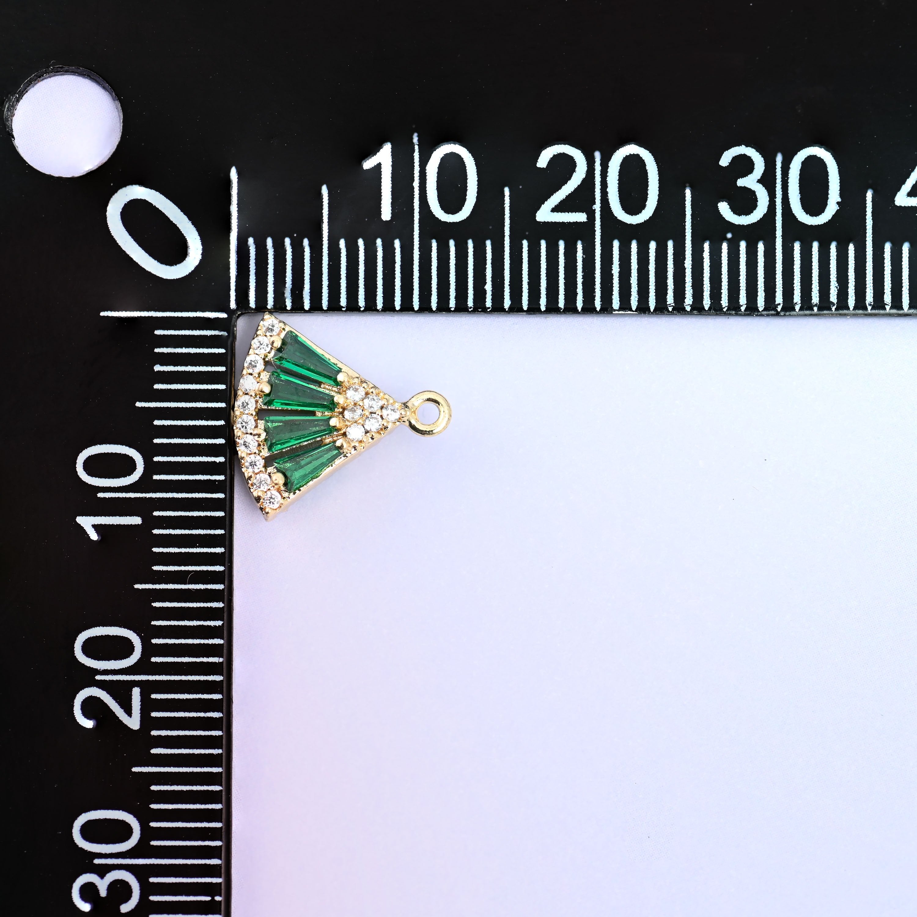 Small gold charms, one green fan charm measured against a millimetre ruler