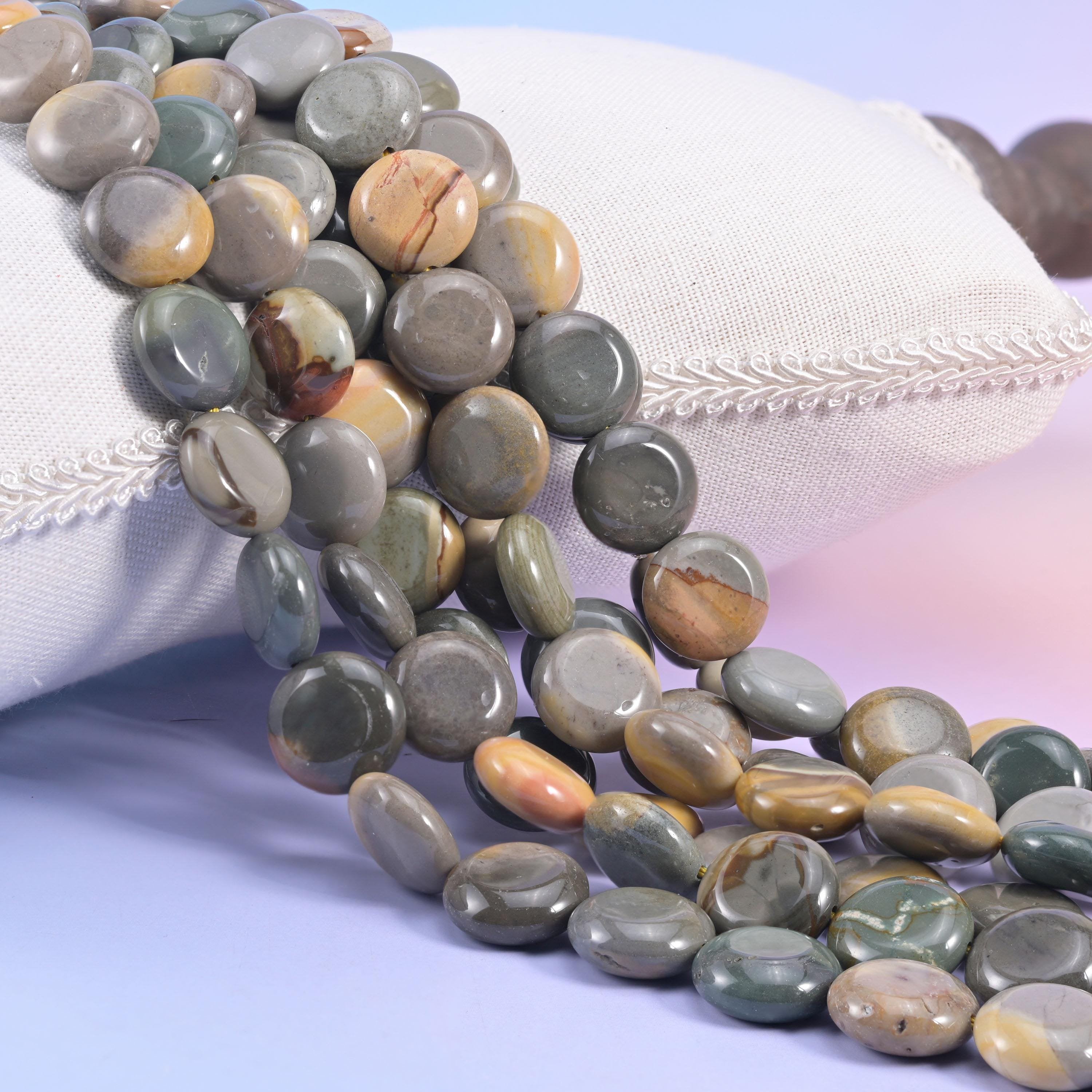 Picture jasper coin strands spilling from a cream cushion, slate grey discs banded with caramel