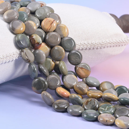 Picture jasper coin strands spilling from a cream cushion, slate grey discs banded with caramel