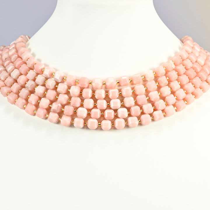 Natural pink opal faceted cube strands set as a layered collar on a white neck display bust, salmon cubes banked across the throat.