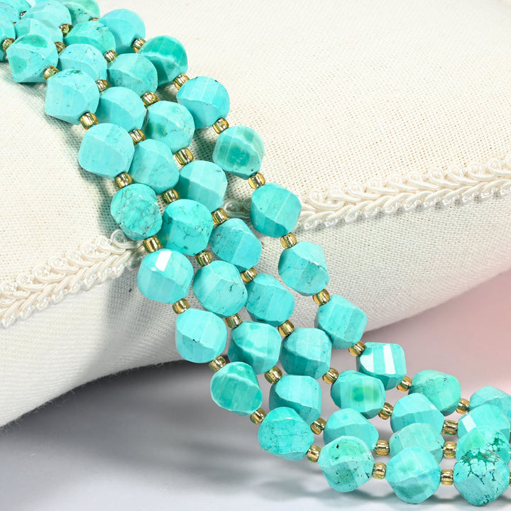 Dyed blue green howlite faceted spiral twist beads 10mm with small gold spacer beads, several strands draped over a white cushion