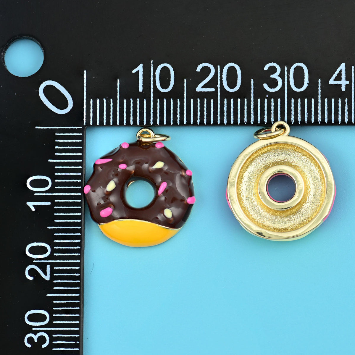 Sprinkle donut charm and its plain gold back on a millimetre ruler, showing size and thickness.