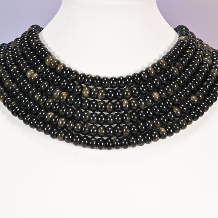 Multi-strand Gold Obsidian necklace laid flat on a mannequin neck form against a lavender background.