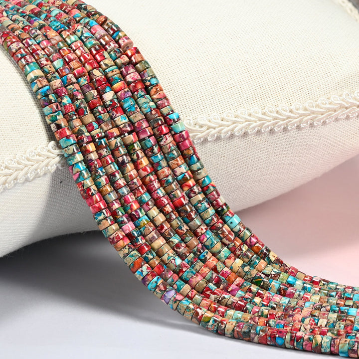 Dyed pink blue sea sediment jasper heishi disc beads 2x4mm, several strands of raspberry pink, red and turquoise discs draped over a white cushion