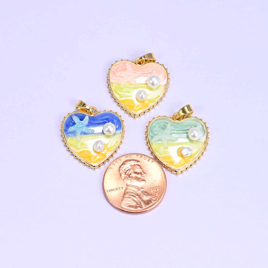 Enamel Heart Pendants beside a US penny for scale, with the pink, blue and green charms each measuring roughly 20mm across.