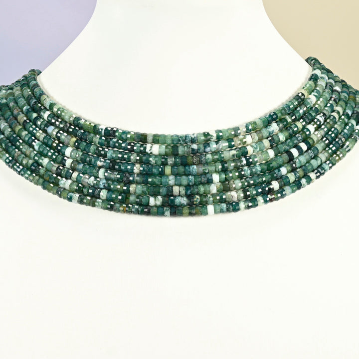Moss agate faceted heishi disc strands arranged as a layered collar on a white display bust, dark green beads across the neck