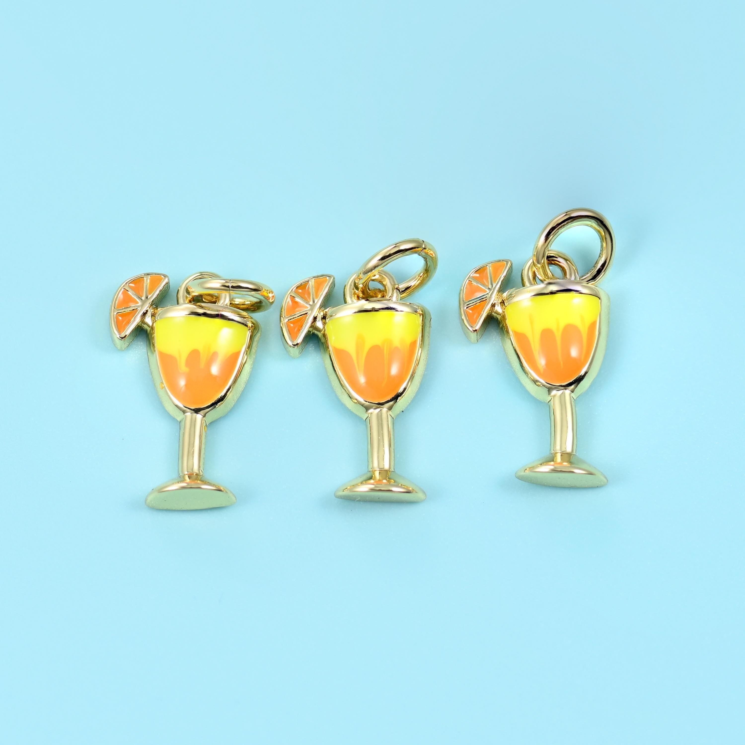 A stemmed cocktail glass filled with glossy sunset-orange and yellow enamel, an orange slice enamelled onto the rim, and…