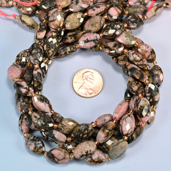 Rhodonite faceted flat oval beads 9x14mm coiled in a loop around a US penny for scale, close-up of the faceted flat oval shape