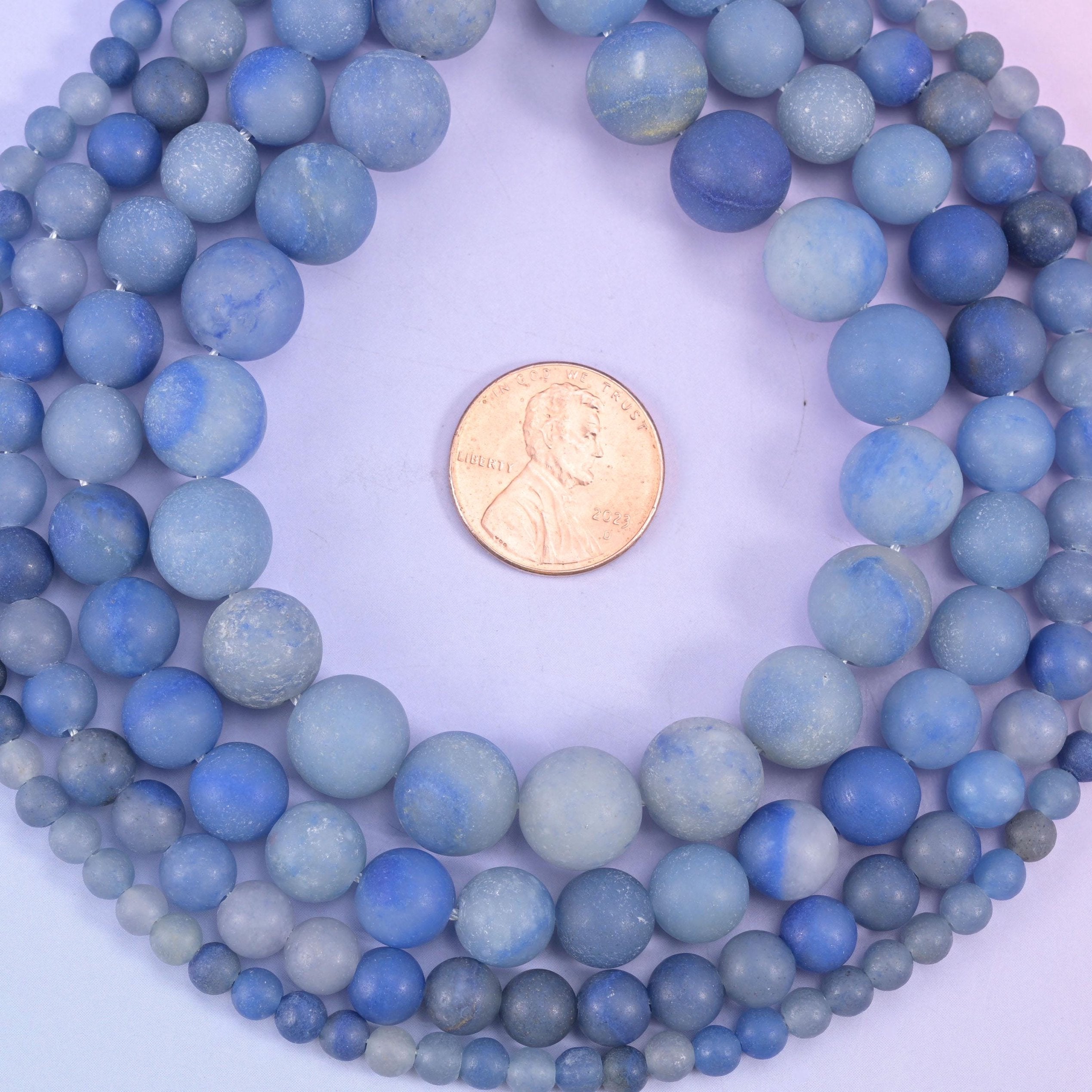 Denim blue rounds finished matte all over, so the surface reads soft and chalky rather than shiny. Pale grey-blue clouding drifts through the darker stone and gives the whole strand a faded