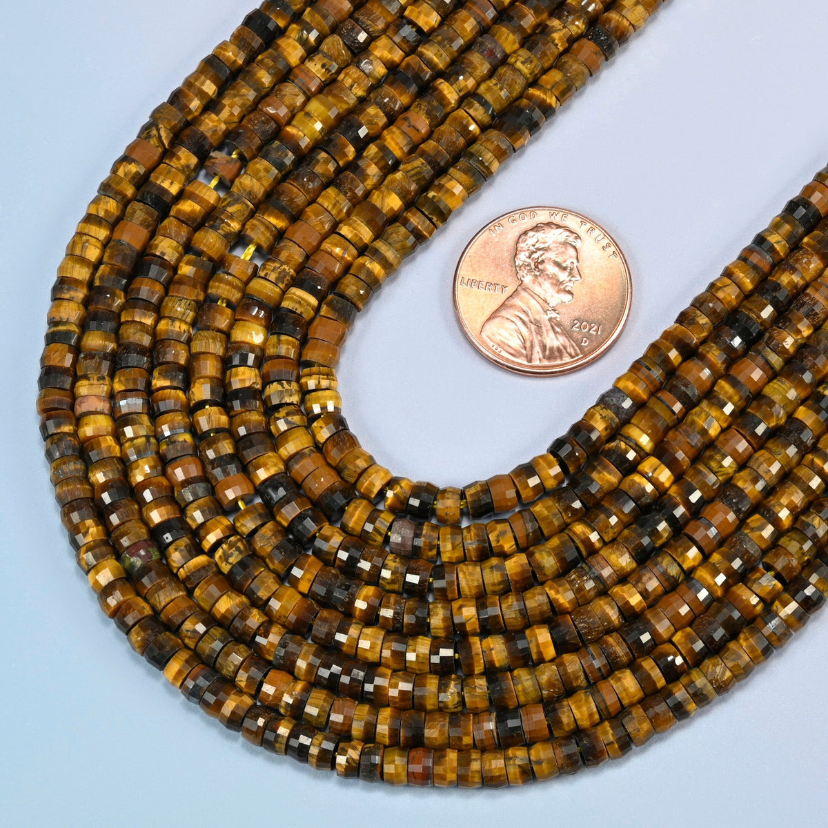 Close view of tiger eye faceted heishi disc strands curving beside a US penny for scale