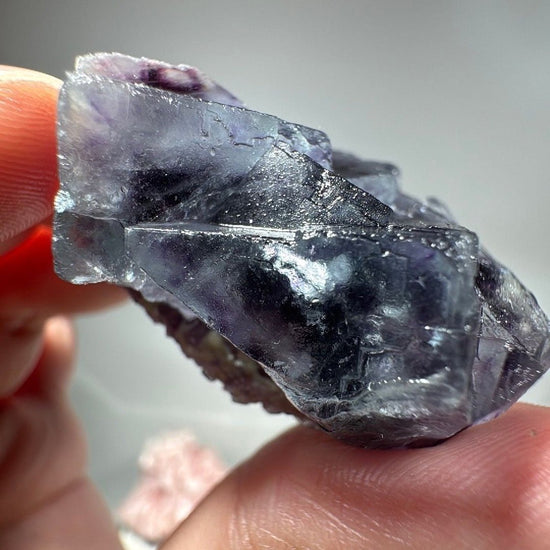 Long profile of the purple Fluorite specimen resting between fingertips