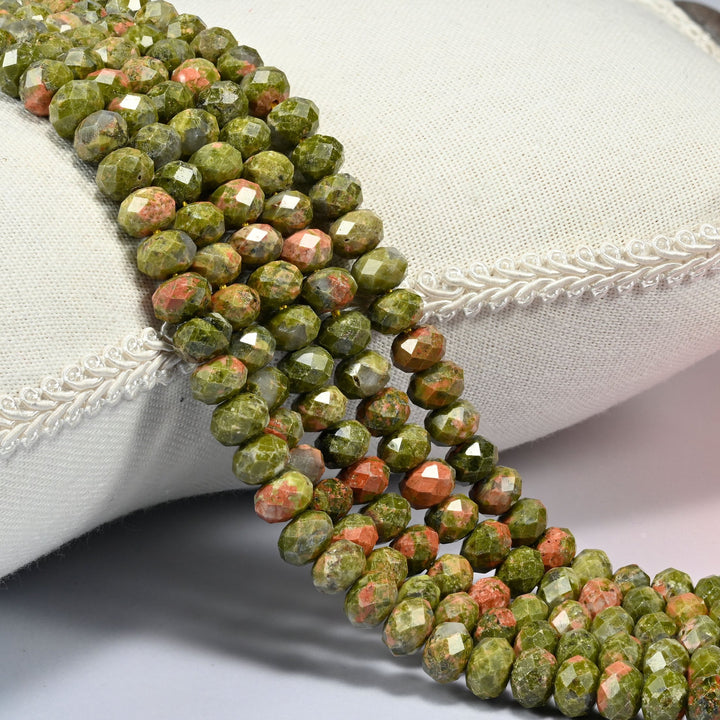 Unakite faceted rondelle beads 5x8mm in olive green blotched with salmon pink, several strands draped over a white cushion
