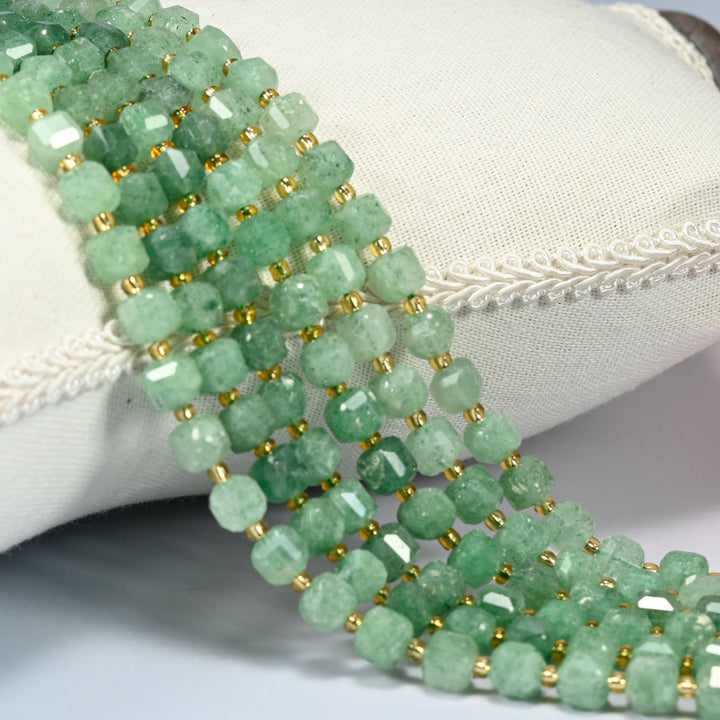 Natural green strawberry quartz faceted cube strands draped over a white linen cushion, soft green beads with gold glass spacers