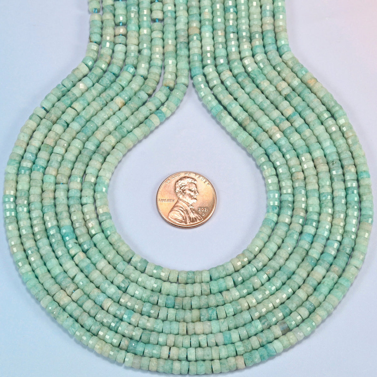Green amazonite faceted heishi disc strands formed into a teardrop loop around a US penny for scale