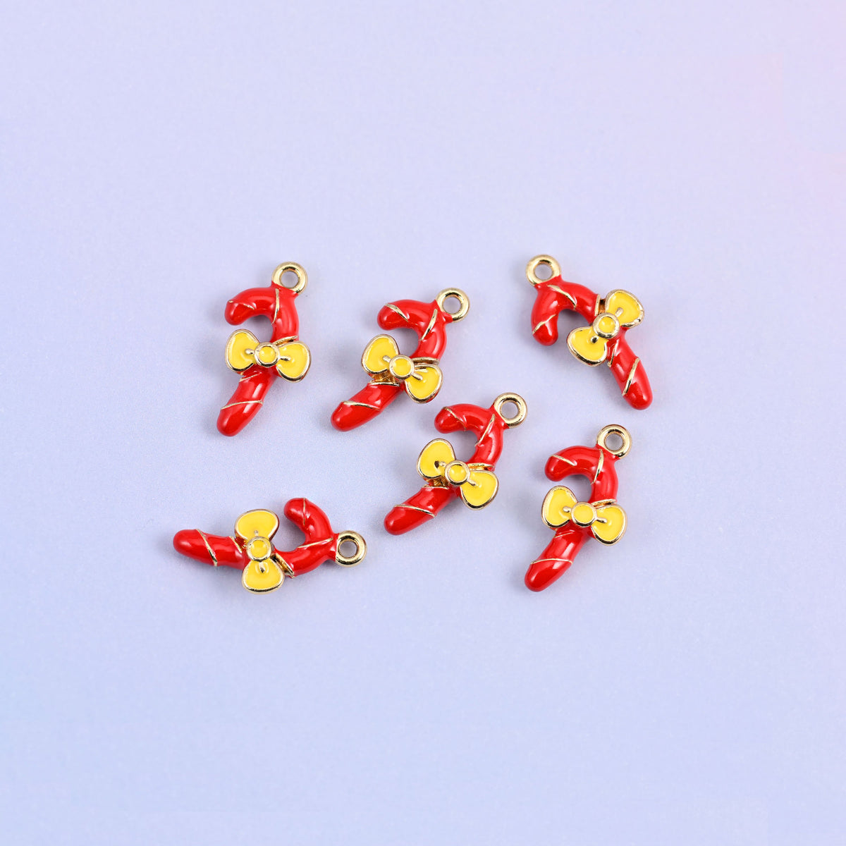 Seven red candy cane charms scattered in a group, enamel over 18K gold plated brass with yellow bows.