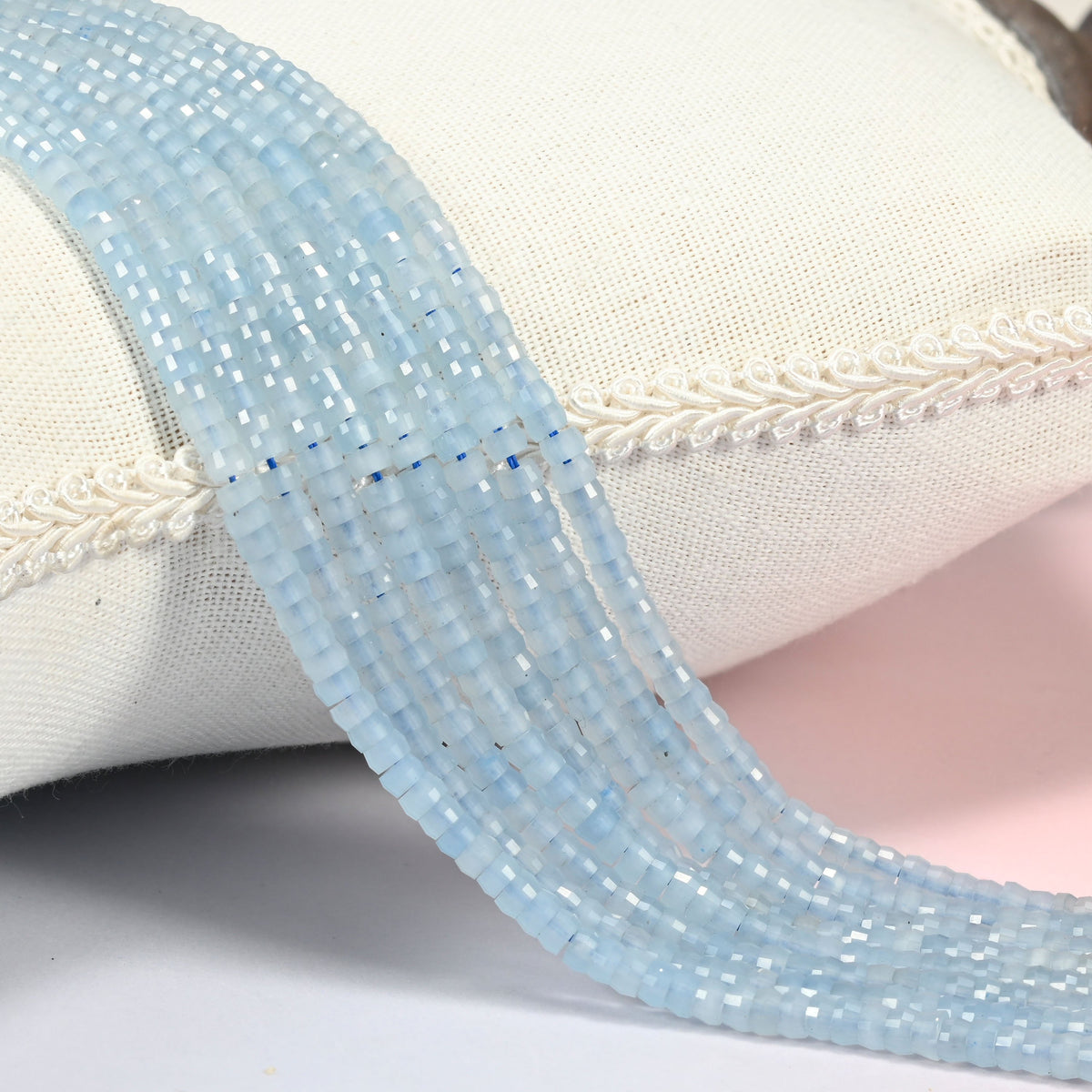 Aquamarine chalcedony faceted heishi disc beads 2x4mm, several strands draped over a white cushion