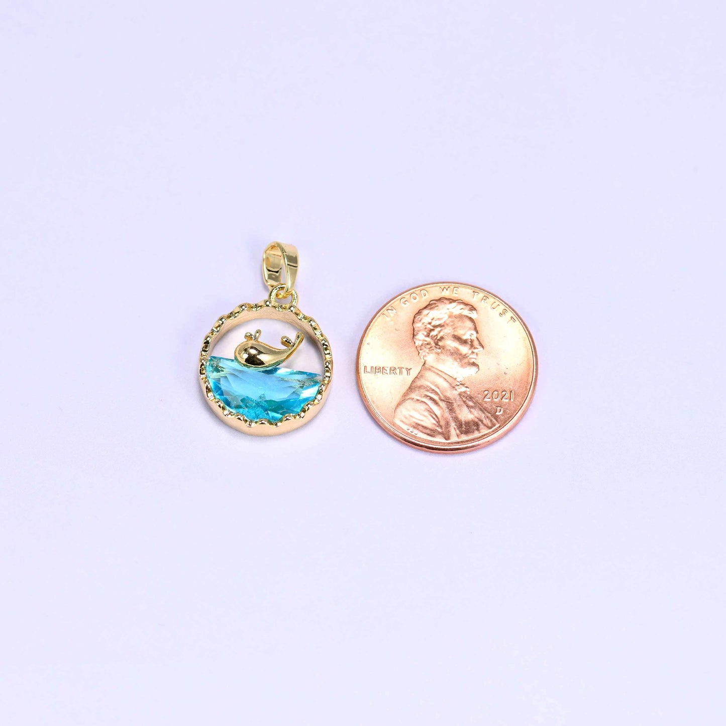 Whale charm with a gold whale silhouette diving into a faceted blue zirconia wave