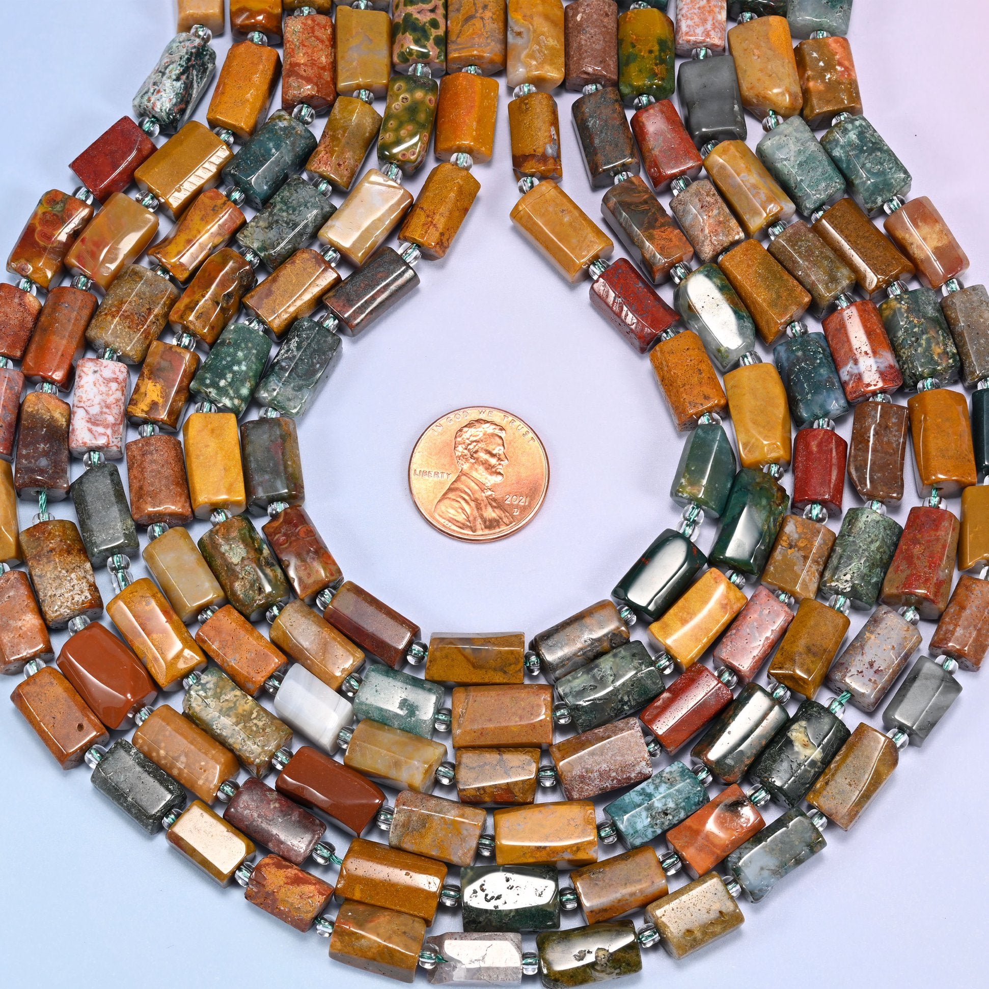 Bundled coil of faceted Ocean Jasper tube beads on a lavender background with a penny placed at the center for scale.