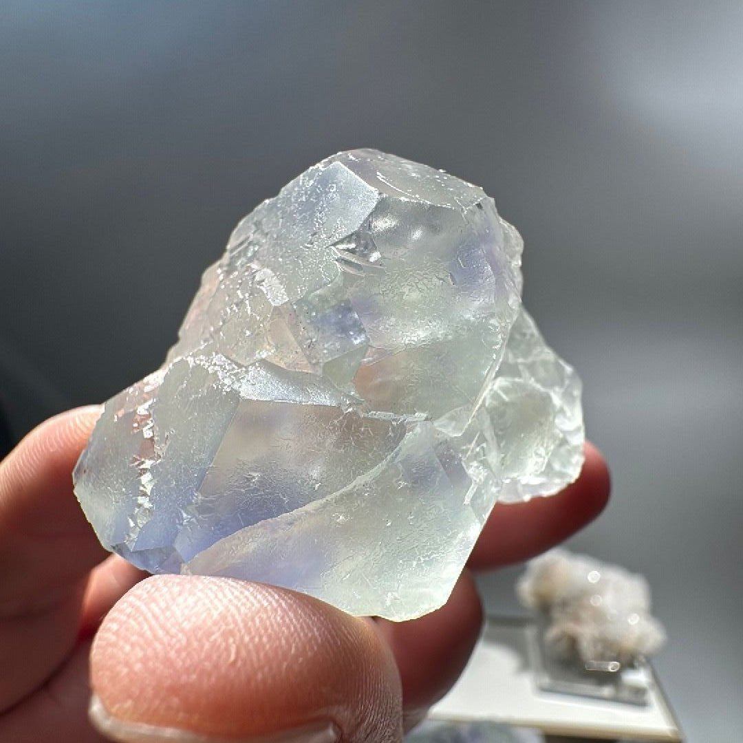 Pale green cubic fluorite crystal held in fingertips, violet-blue zoning inside