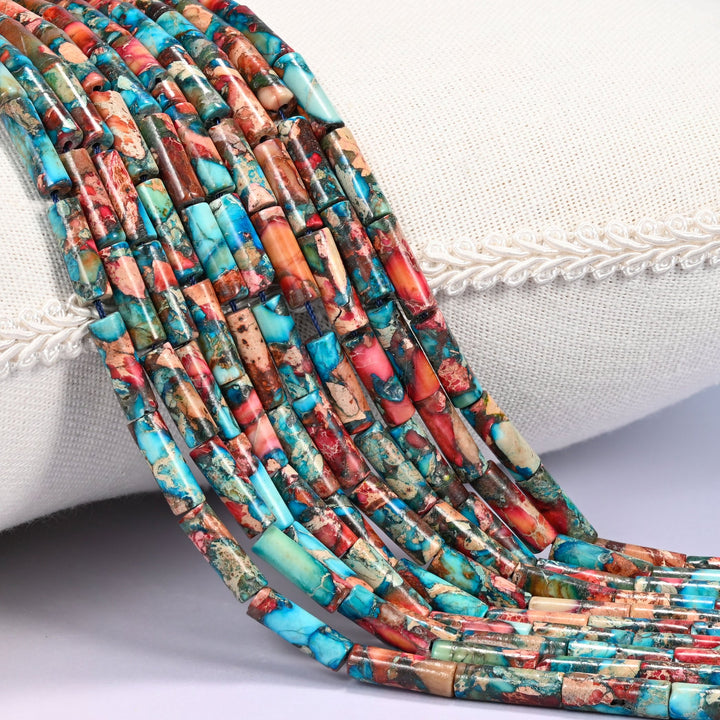 Close-up of multiple strands of turquoise, coral red, and brown dyed Sea Sediment Jasper tube beads draped over a cream fabric jewelry display bust.