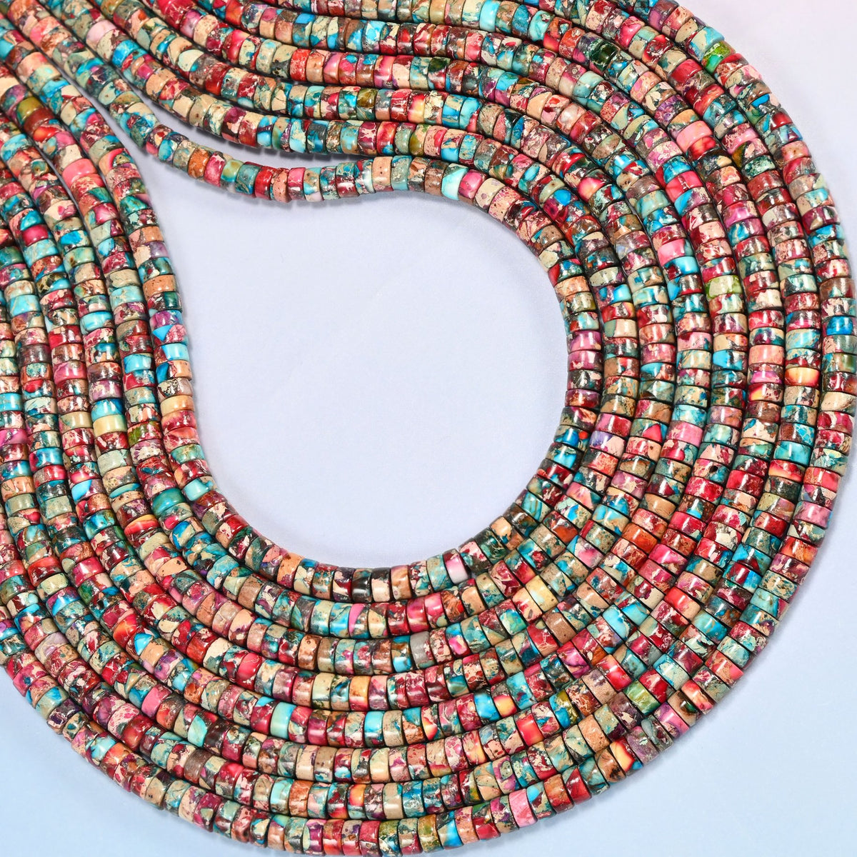 Dyed pink blue sea sediment jasper heishi disc beads 2x4mm curved into an open loop, showing the pink and turquoise mix across whole strands